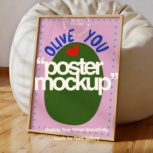 May include: A framed poster with a pink background and a large green olive shape. The poster reads "OLIVE YOU" in blue, with a red heart and the words "poster mockup" in white. The frame is a light wood color.