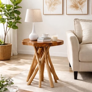 Puede incluir: Una mesa auxiliar redonda de madera con acabado natural. La tapa es de color marrón claro y tiene una forma única. La base está hecha de ramas de madera entrelazadas. Una lámpara blanca, libros y una vela están encima.