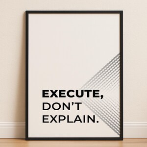 May include: Black framed wall art with the text "EXECUTE, DON'T EXPLAIN." The artwork features a white background with a diagonal gray and white geometric design in the upper right corner. The frame is black.