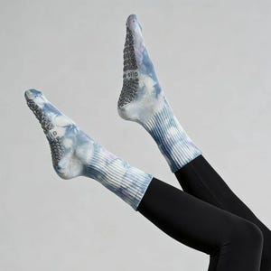 Può includere: Calzini tie-dye nei toni del blu, viola e bianco. I calzini hanno un polsino a coste e un'aderenza strutturata sulla suola. Indossati con leggings neri.