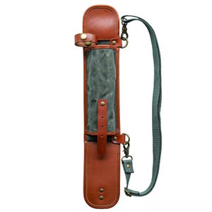 May include: A brown leather and canvas carrying case with a green strap. The case has a rectangular shape with a flap and a buckle closure. The interior is lined with green canvas. The case has a shoulder strap and metal hardware.