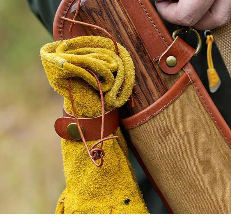 May include: Close-up of a leather quiver with a rolled yellow glove secured by a brown leather strap. The quiver has a wooden back and a canvas front with brown leather trim. A small yellow tool hangs from a brass ring.