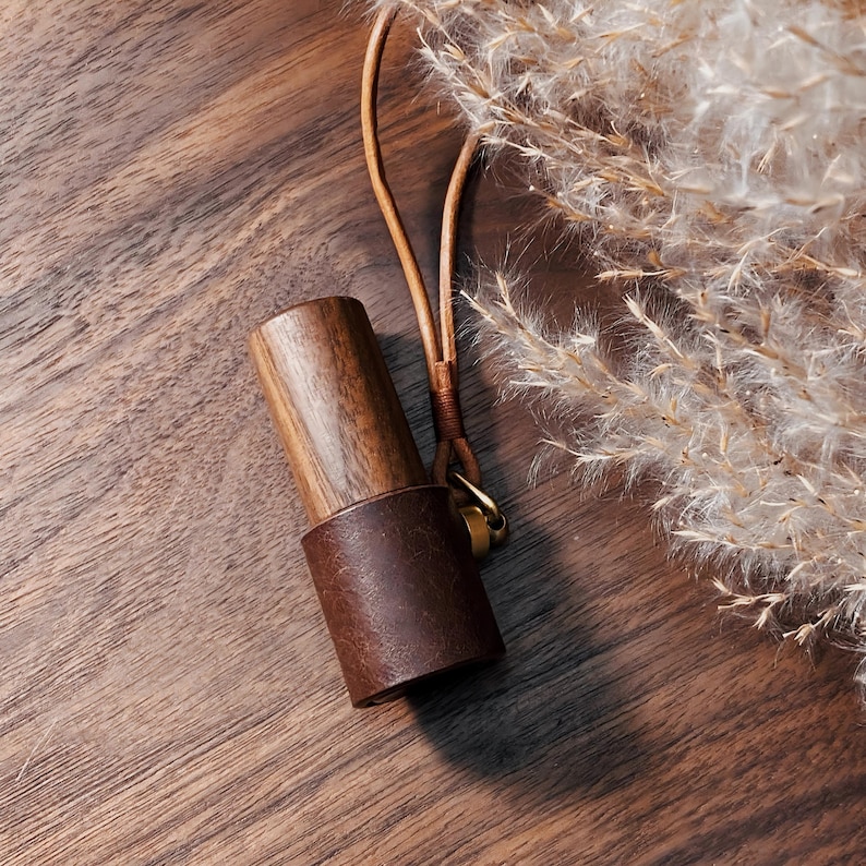 May include: A wooden and leather accessory with a brown leather band and a wooden top. The accessory has a leather strap with a gold-colored clasp. The background is a wooden surface with dried plants.
