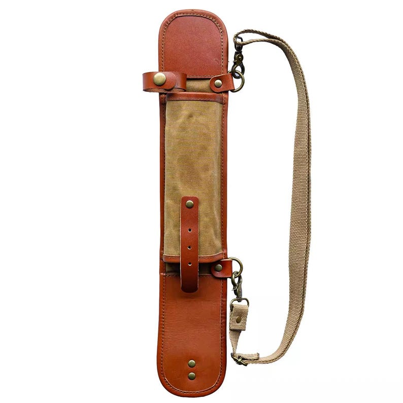 May include: A brown leather and canvas carrying case with a shoulder strap. The case has a rectangular shape with a flap closure and a tan canvas center. The shoulder strap is a light brown color and is attached with metal clasps.