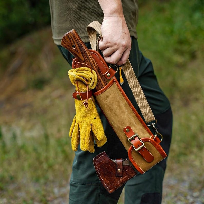 May include: Axe with a wooden handle and a leather sheath. The sheath is tan and brown with a shoulder strap. A pair of yellow gloves is attached to the sheath. The axe head is protected by a brown leather cover.