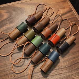 May include: A collection of wooden aromatherapy diffusers with leather accents in various colors, including brown, green, and orange. Each diffuser has a leather strap for carrying. The diffusers are arranged on a wooden surface.