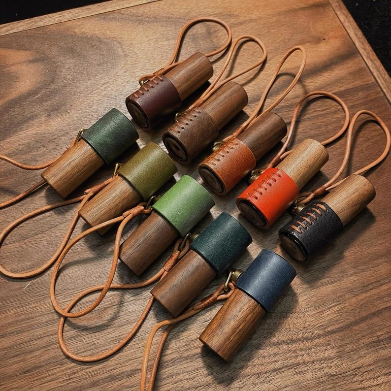 May include: A collection of wooden aromatherapy diffusers with leather accents in various colors, including brown, green, and orange. Each diffuser has a leather strap for carrying. The diffusers are arranged on a wooden surface.