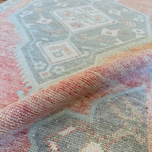 Könnte beinhalten: Ein langer Läufer mit einem weichen pfirsich- und korallenfarbenen Hintergrund und sich wiederholenden geometrischen Medaillonmustern in gedecktem Grau und Weiß. Das Textil hat eine strukturierte, gewebte Oberfläche mit einer umgeschlagenen Ecke.