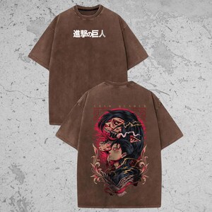 May include: A brown short-sleeve t-shirt featuring the white Japanese text 進撃の巨人 on the front chest. The back displays a detailed graphic illustration of a character with dark hair and a skeletal figure, accented by red and gold floral elements.