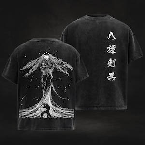 May include: Two black t-shirts. The front shirt features a white illustration of a tall figure with flowing hair and a person kneeling. The back shirt has white Japanese characters. The shirts have a vintage, faded look.