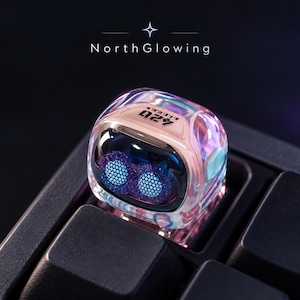 Puede incluir: Una tecla de teclado mecánico translúcida e iridiscente con forma de cubo redondeado. La superficie superior muestra el texto 420, mientras que la cara frontal revela dos ojos circulares, morados, brillantes y con textura de malla en una cavidad.