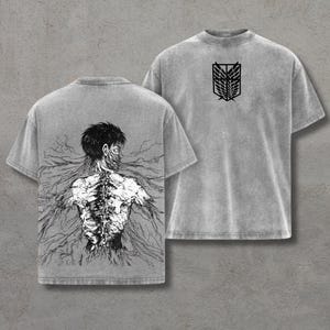 Może przedstawiać: Dwie szare koszulki. Jedna przedstawia czarno-białą ilustrację pleców postaci z odsłoniętym kręgosłupem i korzeniami. Druga koszulka ma czarny emblemat z przodu. Obie mają krótkie rękawy.