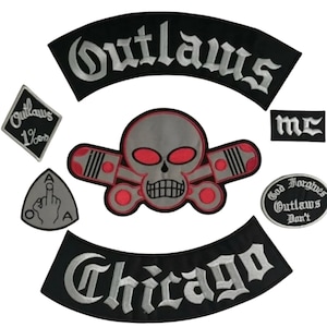 May include: A collection of black and gray embroidered patches. The patches feature the words "Outlaws" and "Chicago" in white script, a skull with red eyes, and other motorcycle club symbols.