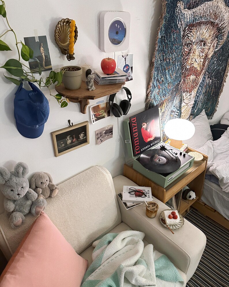 K&ouml;nnte beinhalten: Gem&uuml;tliches Zimmer mit wei&szlig;em Sofa, einem Nachttisch aus Holz mit Plattenspieler und einem Wandteppich von Van Gogh. Ein Regal zeigt eine Pflanze, einen roten Apfel und einen CD-Player. Pl&uuml;schhasen und ein rosa Kissen liegen auf dem Sofa.