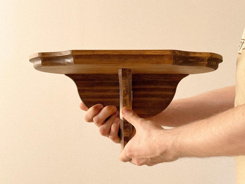 K&ouml;nnte beinhalten: Ein Regal aus dunkel gebeiztem Holz mit dekorativer Kante und Halterung. Das Regal wird gehalten. Es ist f&uuml;r die Wandmontage konzipiert. Die Abmessungen betragen ca. 30 cm Tiefe.