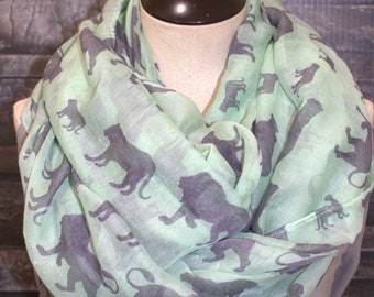 May include: A light green scarf with a repeating pattern of dark grey animal silhouettes. The animals include lions, monkeys, and leopards.
