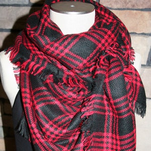 May include: A black and red plaid scarf with fringe. The scarf is folded and draped over a mannequin.