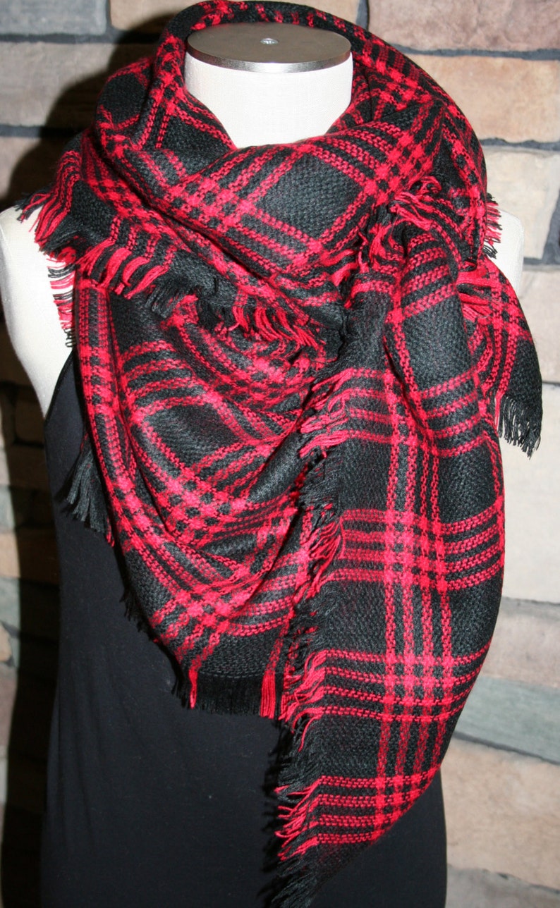 May include: A black and red plaid scarf with fringe. The scarf is folded and draped over a mannequin.