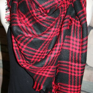 May include: A black and red plaid scarf with fringe edges. The scarf is folded and draped over a mannequin.