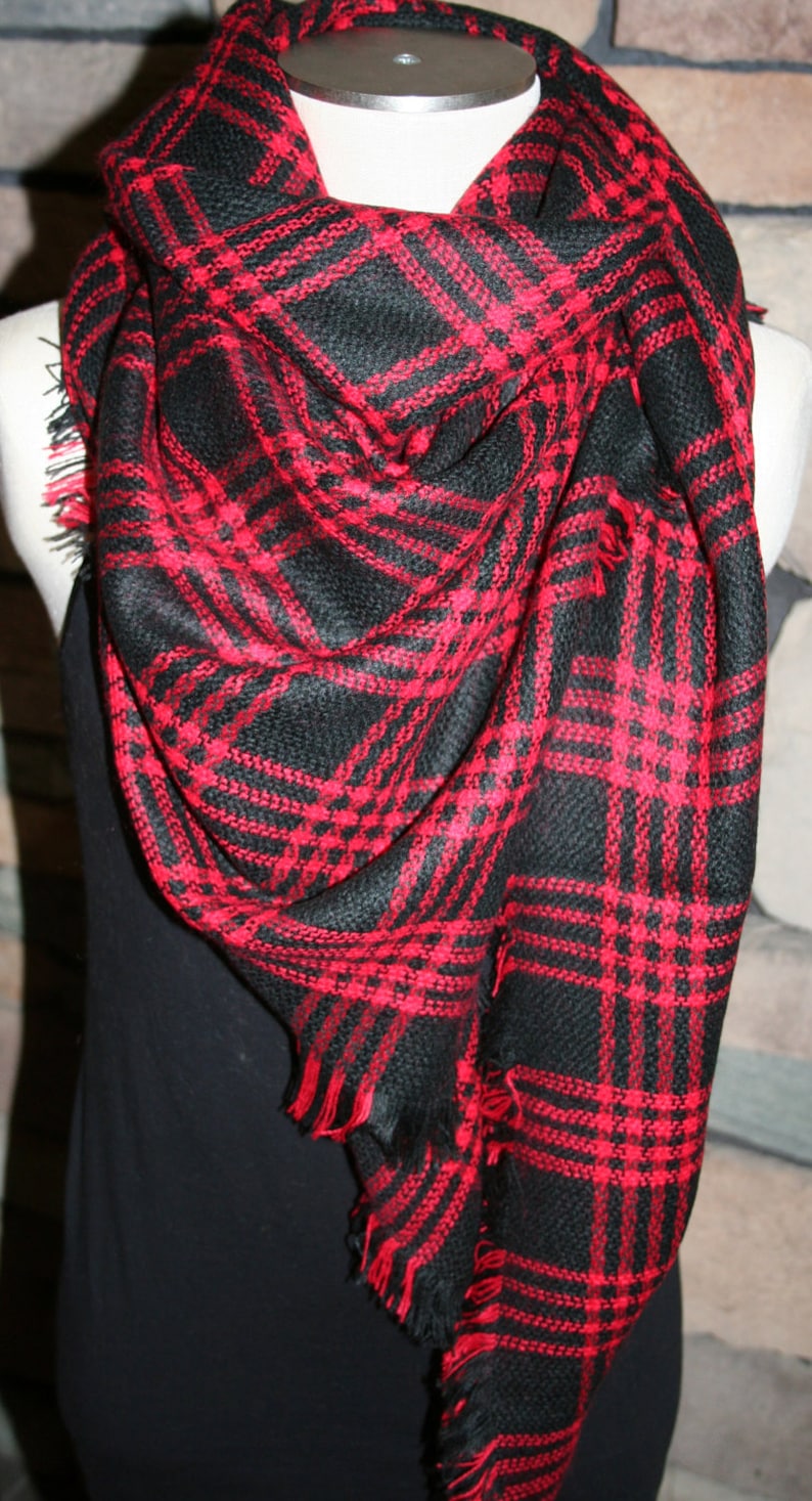 May include: A black and red plaid scarf with fringe edges. The scarf is folded and draped over a mannequin.