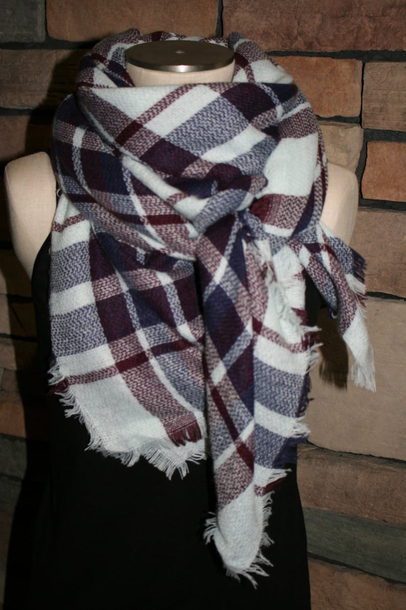 Op de afbeelding: Een witte, bordeauxrode en donkerblauwe geruite sjaal met rafelige randen. De sjaal is gevouwen en gedrapeerd om de nek van een mannequin.