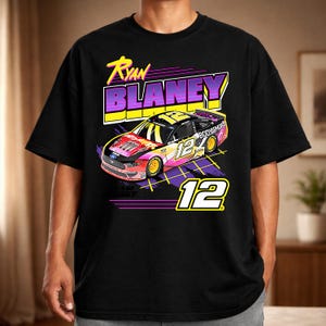 May include: Black t-shirt featuring a colorful graphic of a race car with the number 12 and the name "Ryan Blaney". The design includes the text "BODYARMOR" and a retro-style font.