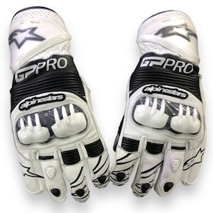 Könnte beinhalten: Ein Paar weiß-schwarze Alpinestars GP Pro Motorradhandschuhe. Die Handschuhe haben eine weiße Lederbasis mit schwarzen Akzenten, einschließlich des Markennamens und -logos. Sie haben einen Schutzpolster an Knöcheln und Fingern.