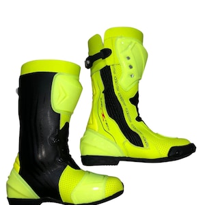 May include: Pair of neon yellow and black motorcycle boots. The boots have a tall design with protective panels and a perforated toe area. The boots have a black buckle and a black sole. The boots are designed for safety and performance.