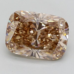 May include: A cushion-cut gemstone with a warm, light brown champagne hue. The stone features a complex arrangement of triangular and trapezoidal facets that create a high degree of light reflection and internal brilliance across its surface.