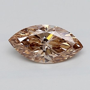 May include: A marquise-cut gemstone with a warm, light brown hue. The stone features a faceted surface that creates a complex pattern of light and dark reflections across its elongated, pointed shape, showcasing a brilliant, polished finish.