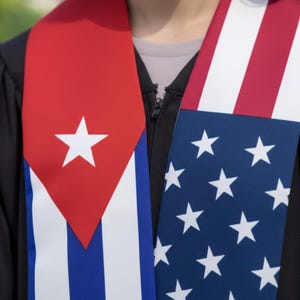 May include: A graduation sash featuring the flags of Cuba and the United States. The Cuban flag side has a red triangle with a white star and blue and white stripes. The American flag side has white stars on a blue background with red and white stripes.