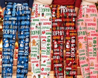 May include: Four pairs of lounge pants featuring a repeating pattern of the name Sophia, snowmen, gingerbread men, and holiday icons. The pants come in blue plaid, white, red plaid, and pink, each with a white drawstring waist and side pockets.