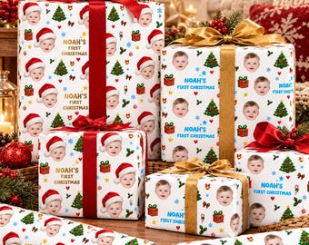 May include: Custom wrapping paper featuring a repeating pattern of a baby wearing a Santa hat, green Christmas trees, and gift boxes, with the text "NOAH'S FIRST CHRISTMAS" printed in blue or gold on white paper rolls and gift boxes.