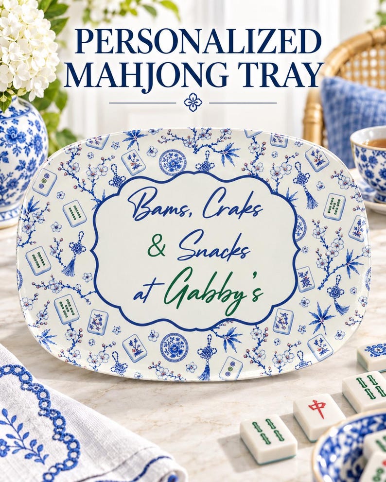 Puede incluir: Una bandeja de servicio ovalada de cer&aacute;mica blanca con un patr&oacute;n floral azul intercalado con peque&ntilde;as ilustraciones de fichas de mahjong. El centro muestra el texto "Bams, Craks & Snacks at Gabby's" en una fuente cursiva azul y verde.