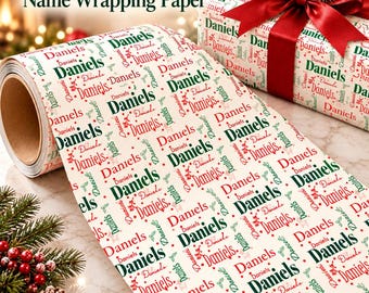 May include: A roll of cream-colored wrapping paper featuring a repeating pattern of the name Daniels in alternating dark green and red script and serif fonts, with a gift box wrapped in the same paper and topped with a red ribbon.
