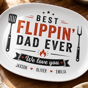 May include: An oval white ceramic platter featuring black and orange text that reads BEST FLIPPIN' DAD EVER. The design includes a black spatula and fork on the sides, a flame icon, and a banner with the text We love you and names JAXSON, OLIVER, EMILIA.
