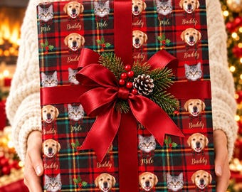 May include: A rectangular gift box wrapped in red, green, and black plaid paper featuring repeating portraits of a golden retriever labeled Buddy and a tabby cat labeled Milo. A large red satin ribbon bow with pine needles and berries.
