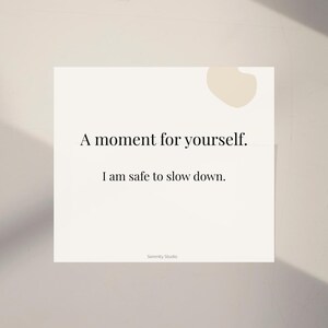 Op de afbeelding: Een witte kaart met de tekst "A moment for yourself. I am safe to slow down." in een minimalistisch lettertype. De kaart heeft een lichtbeige abstracte vorm in de rechterbovenhoek en de woorden "Serenity Studio" onderaan.