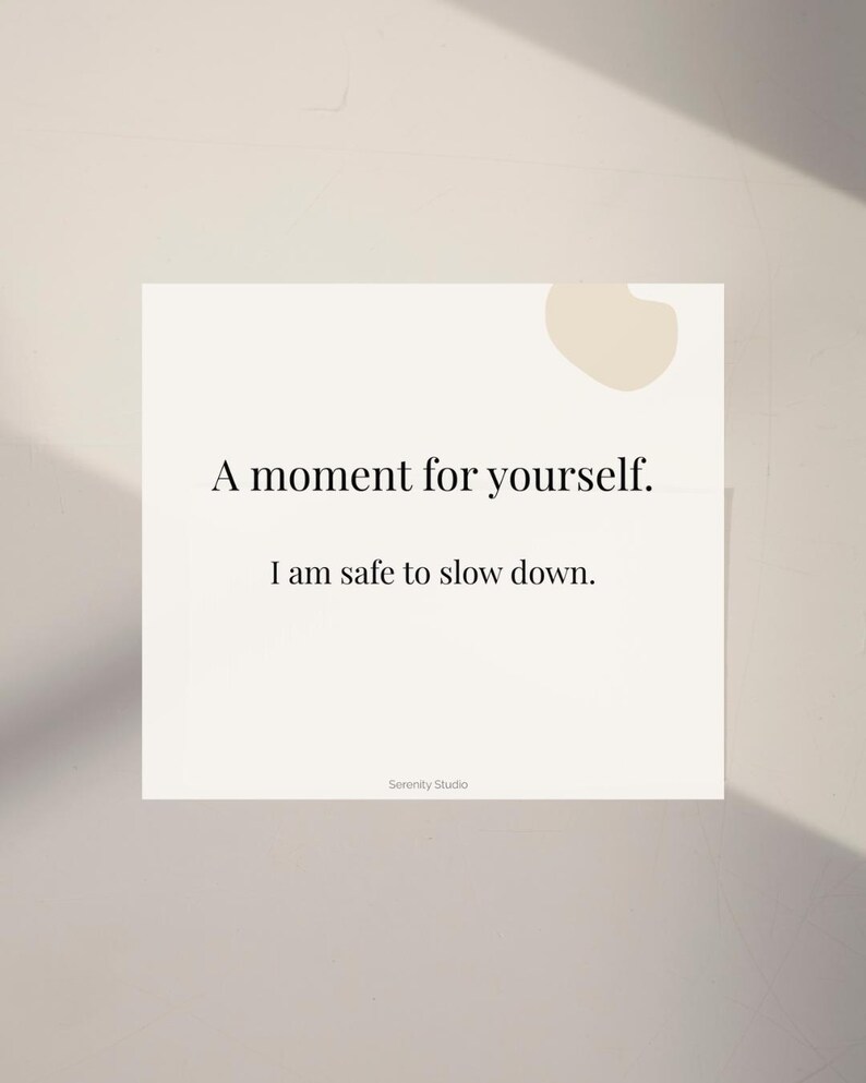 Op de afbeelding: Een witte kaart met de tekst "A moment for yourself. I am safe to slow down." in een minimalistisch lettertype. De kaart heeft een lichtbeige abstracte vorm in de rechterbovenhoek en de woorden "Serenity Studio" onderaan.
