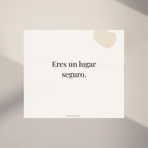 Op de afbeelding: Een witte kaart met de Spaanse tekst "Eres un lugar seguro" in een schreefletter. De kaart heeft een lichtbeige abstracte vorm in de rechterbovenhoek en de woorden "Serenity Studio" onderaan.