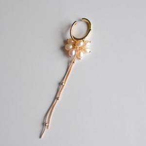May include: A gold-toned ear cuff featuring a cluster of small, iridescent white freshwater pearls. Attached to the pearl cluster are two delicate gold-toned snake chains, each accented with tiny gold beads, hanging down from the ear cuff.