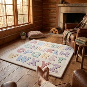 May include: A rectangular area rug featuring a cream-colored base with the English alphabet letters A through Z in a raised, tufted texture. The letters are colored in soft pastel shades of pink, blue, yellow, and green, arranged in rows.