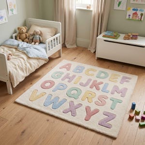 May include: A rectangular area rug featuring the English alphabet in raised, pastel-colored letters against a cream-colored background. The letters are arranged in rows, showcasing a variety of soft hues including pink, blue, yellow, and green.