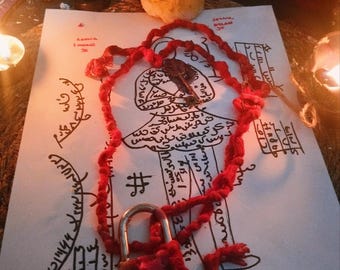 May include: A red cord necklace with a small padlock and a key pendant rests on a sheet of paper with handwritten text and illustrations. A lit candle is in the background, casting a warm glow.