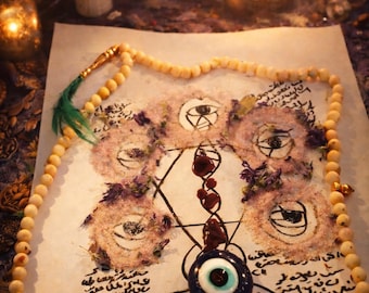 Puede incluir: Una composición mística con un dibujo central de símbolos de ojos, un collar de cuentas y un amuleto de ojo azul. Velas e incienso crean un ambiente espiritual. El dibujo incluye escritura.