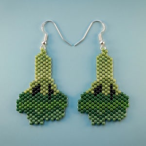 May include: A pair of drop earrings crafted from small green beads in a gradient pattern, transitioning from light green at the top to dark green at the bottom. Each earring features a silver-toned metal hook and a distinct, irregular shape.