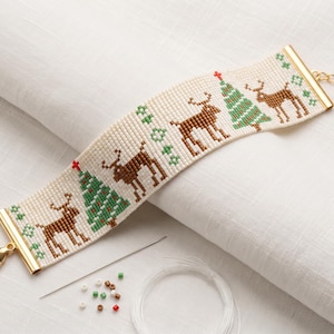 May include: A wide beaded bracelet featuring a repeating pattern of brown reindeer and green Christmas trees on a cream background. The bracelet has gold-tone metal end caps, a lobster clasp, and an extender chain. A needle, thread, and loose beads are included.