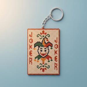 May include: A rectangular keychain featuring a beaded design of a joker playing card. The center displays a jester face in orange, green, and black on a cream background. The word JOKER is printed vertically in red on both sides of the jester.
