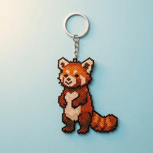 May include: A beaded keyring featuring a red panda design. The red panda is crafted from small, uniform beads in shades of reddish-brown, dark brown, and cream, forming a pixelated appearance. It is attached to a silver-toned metal split ring.