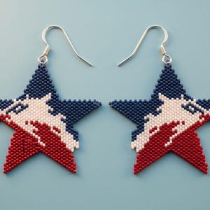 May include: A pair of star-shaped earrings crafted from small beads in a patriotic color scheme. The top section is dark blue, the middle features a white wave-like pattern, and the bottom section is red. Each earring hangs from a silver hook.
